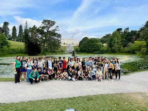 Grande gruppo di ragazzi in posa in un parco, con un laghetto e una villa sullo sfondo