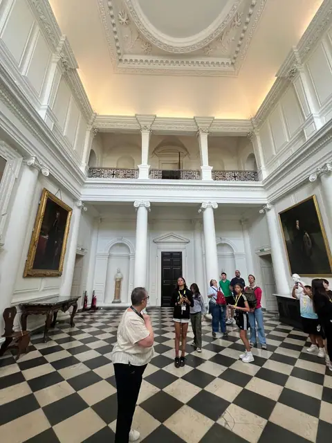 Visita guidata in un salone neoclassico con colonne bianche e pavimento a scacchi