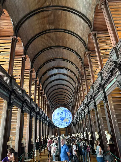 Ragazzi in visita a una biblioteca storica con volta in legno e un grande mappamondo sospeso