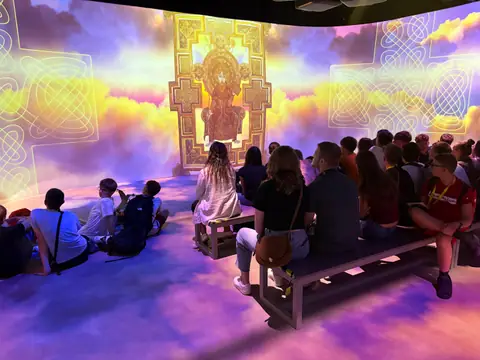 Ragazzi seduti assistono a una proiezione immersiva con motivi celtici e nuvole colorate