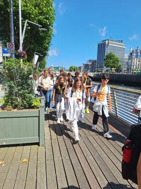 Il gruppo passeggia su una passerella in legno lungo il fiume, in città