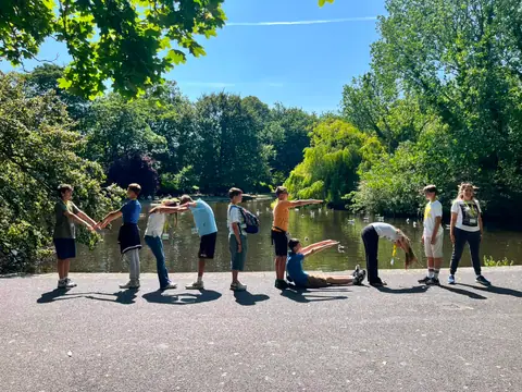 Ragazzi che giocano in fila in un parco, vicino a uno stagno