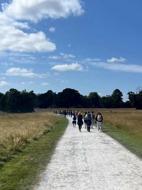 Il gruppo cammina lungo un sentiero sterrato in un grande parco, sotto un cielo azzurro