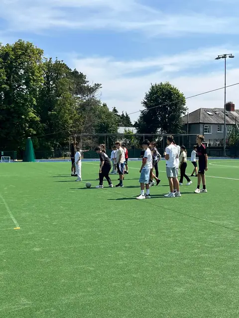 Ragazzi giocano a calcio su un campo in erba sintetica, circondato da alberi