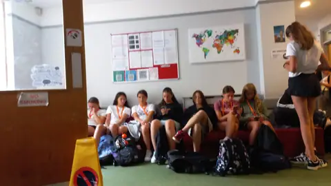 Ragazzi in attesa in una sala della scuola, con una mappa del mondo appesa alla parete